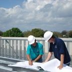 Two ANC Roofing roofers looking over plans on a flat roof