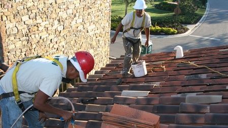 Two people working on a clay tile roof