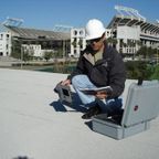 ANC Roofing worker testing a flat rooftop with a football stadium in the background